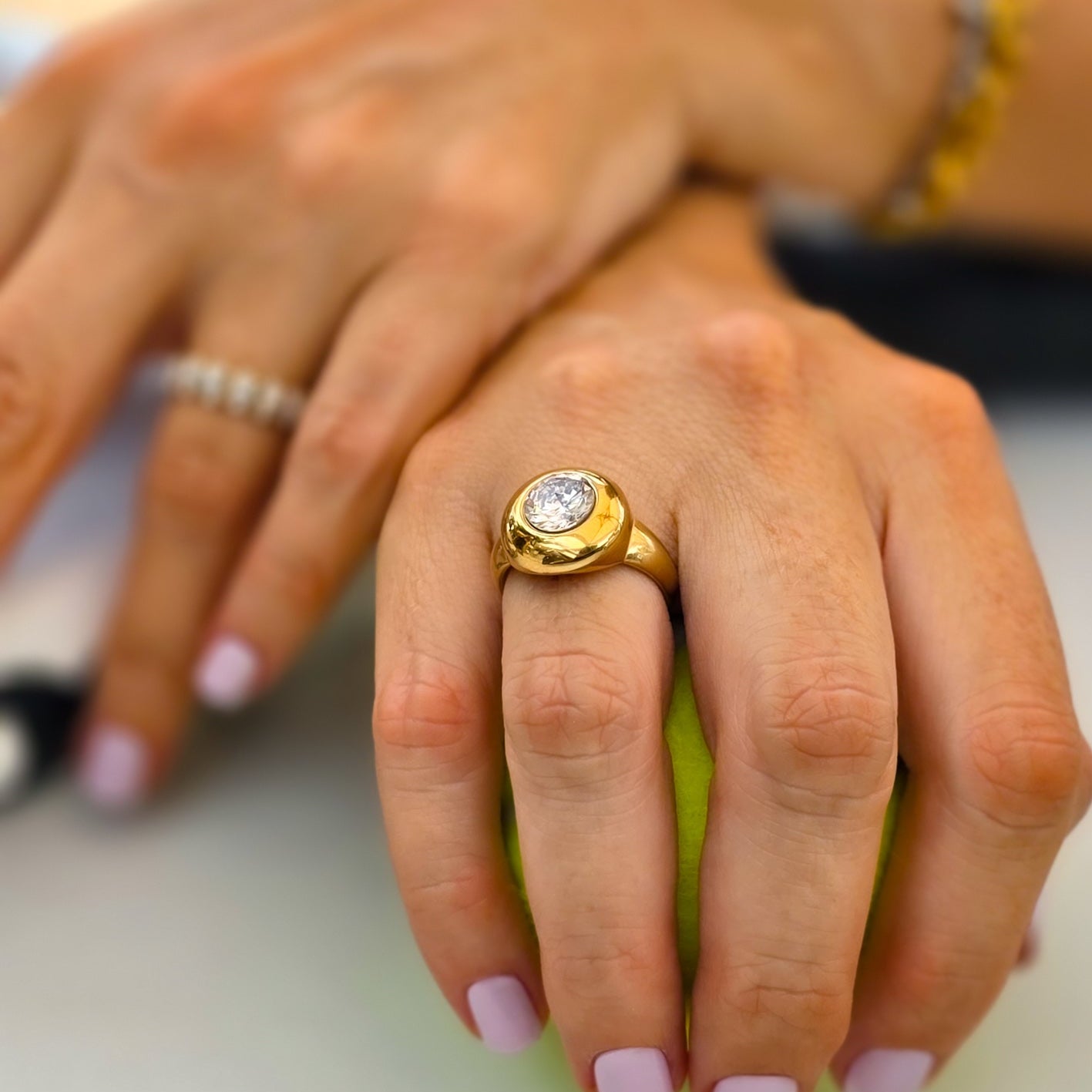 Close-up of hands with a gold ring and pink nail polish holding a green apple.