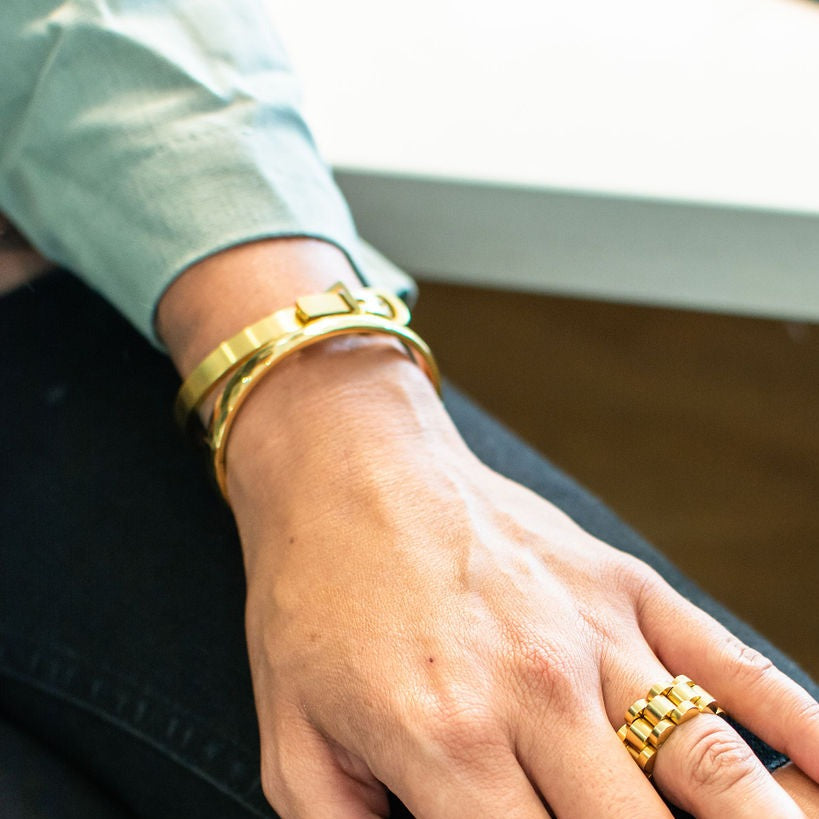 Gold geometric style hard bangle seen on woman's wrist net to other bangle