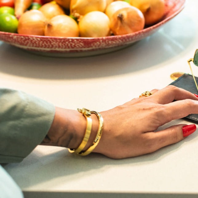 Gold geometric style hard bangle seen on woman's writ net to other bangle