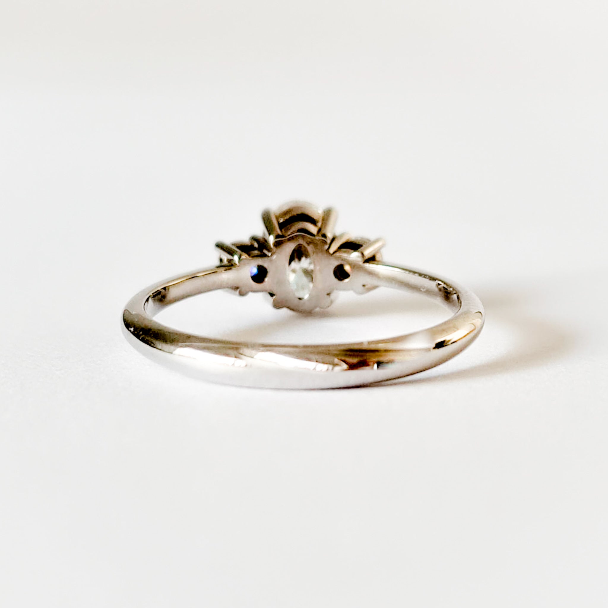Oval and round cut moissanite three stone engagement ring in white gold, back view on white background
