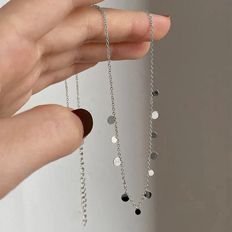 Silver necklace with black accents held by a hand against a neutral background