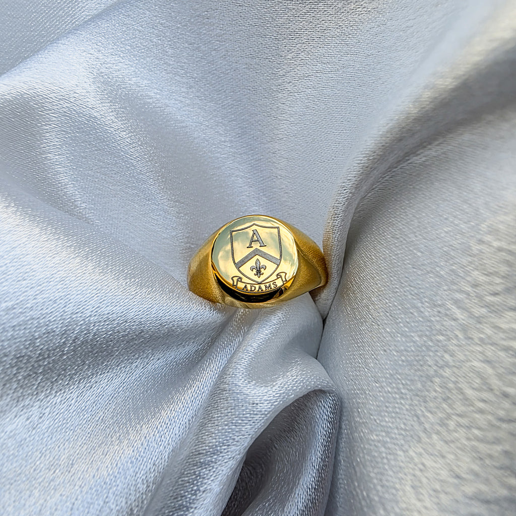Gold ring with emblem design on a light gray fabric background