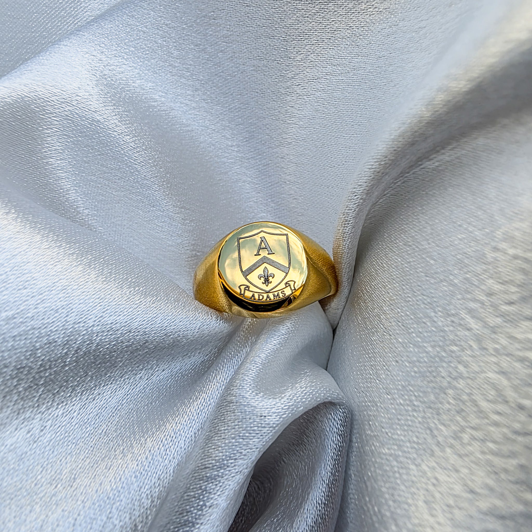 Gold ring with emblem design on a light gray fabric background