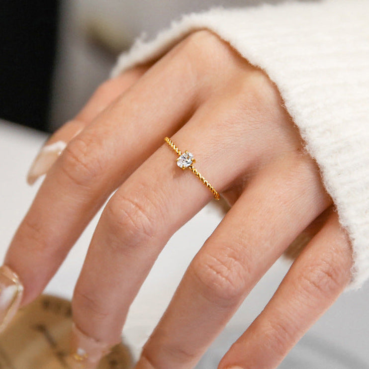 Close-up of a hand wearing a gold ring with a diamond on a neutral background