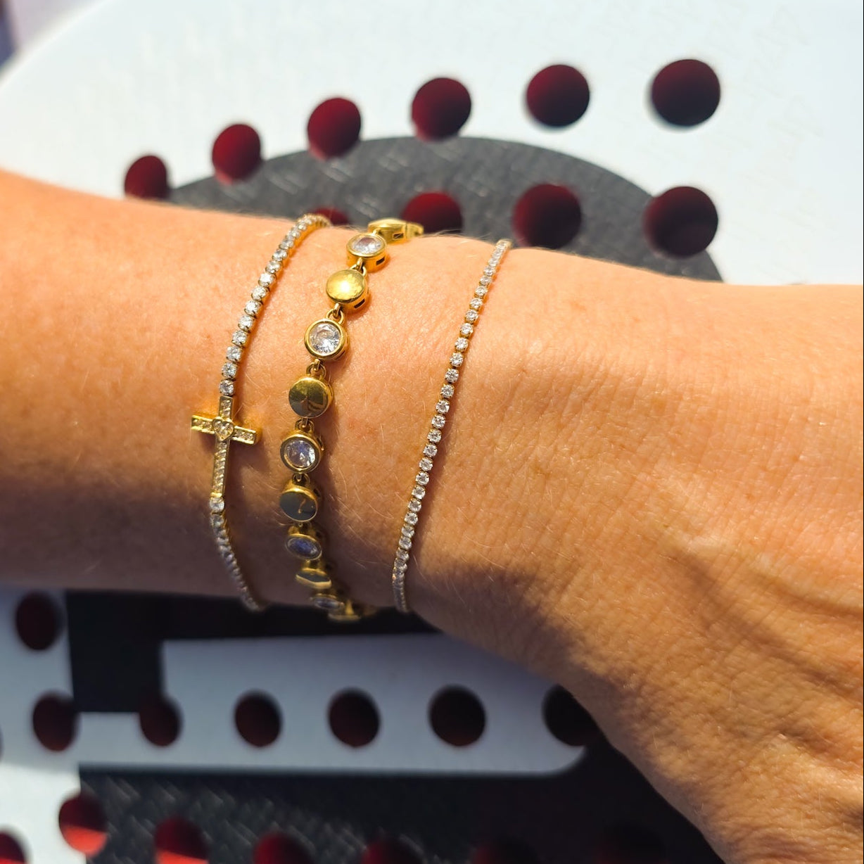 Close-up of a person's arm wearing gold bracelets on a white background with red and black patterns.
