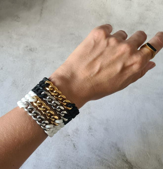 Stack of black, white, gold and silver tone metal and silicone bracelets seen on woman's wrist