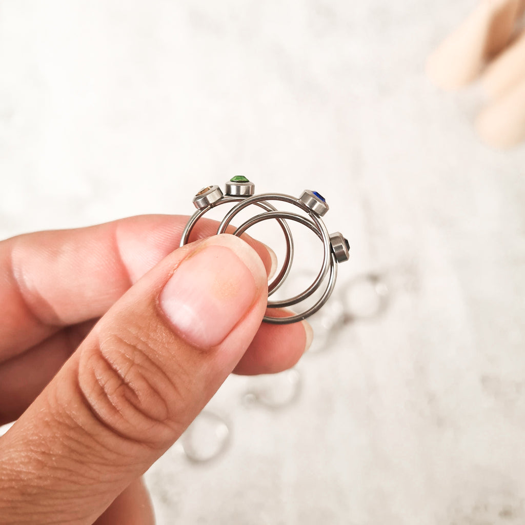 Side view of Stainless steel rings, each set with a coloured cubic zirconia birthstone representing the its month.