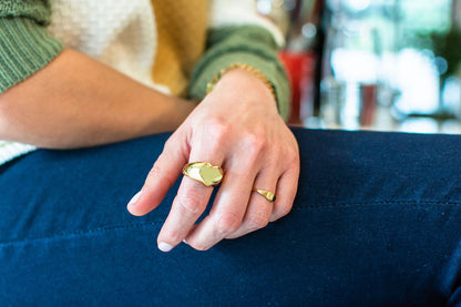 Echo ring in yellow gold styled on hand next to large heart signet ring